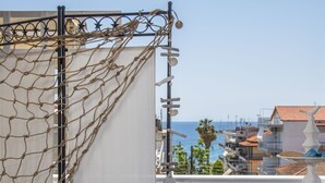 Balcón con mesa dispuesta para el desayuno, con croissants y zumo de naranja, con vistas a una zona costera con edificios y el mar.