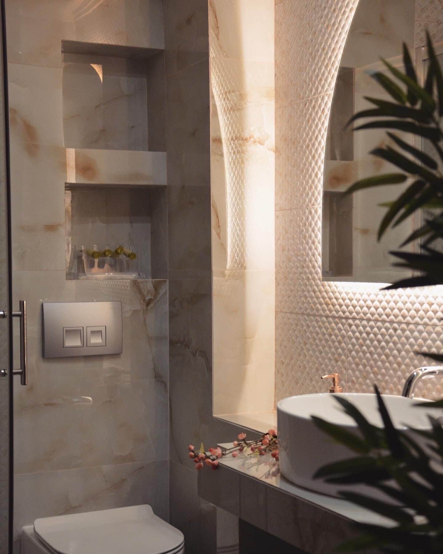 Un baño moderno con pared de mármol, cabina de ducha de vidrio, lavamanos blanco y espejo.