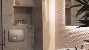 Un baño moderno con pared de mármol, cabina de ducha de vidrio, lavamanos blanco y espejo.