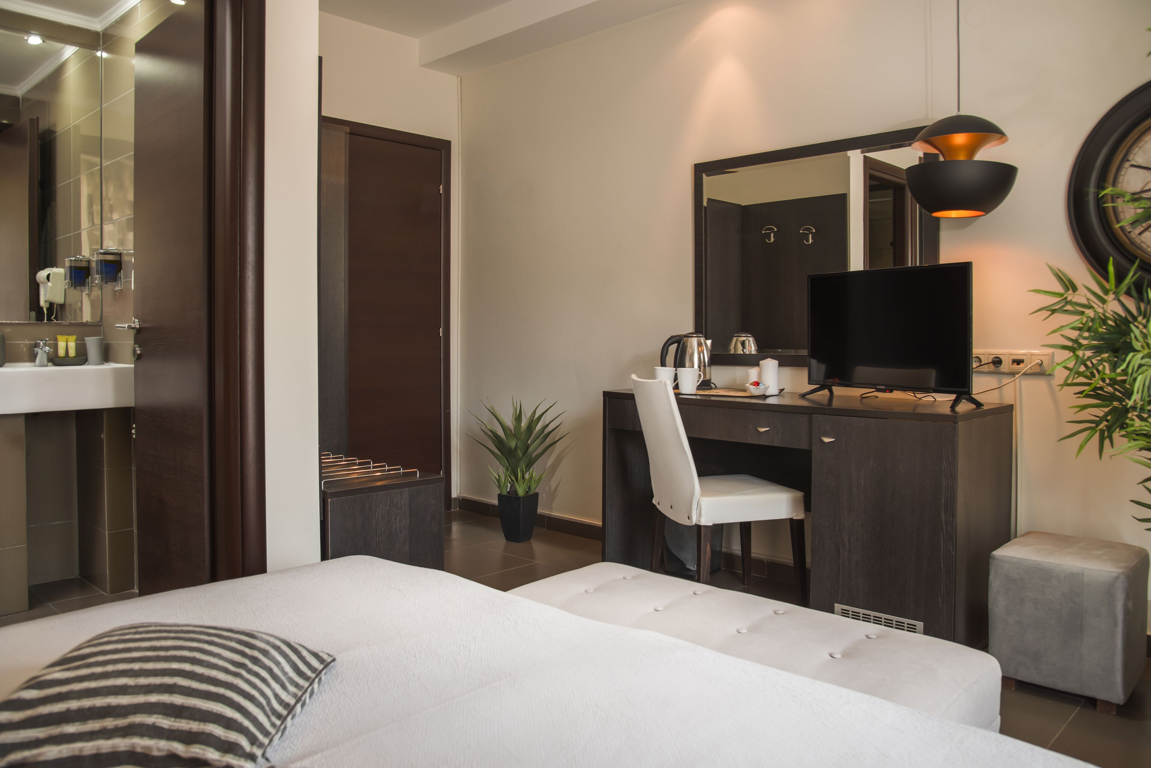 Una habitación de hotel moderna con una cama, un escritorio con silla, un televisor y un espejo grande.