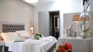 Una cama bien hecha con sábanas blancas y almohadas decorativas, una mesita de noche con lámpara y un frutero en la mesita.