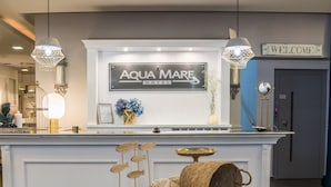Zona de recepción con mostrador blanco, cartel de bienvenida y letrero que dice "Aqua Mare Hotel".