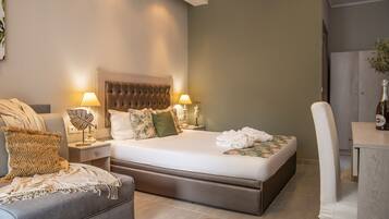 A modern bedroom with a large bed, two bedside tables with lamps, a grey sofa, and a wooden chair.
