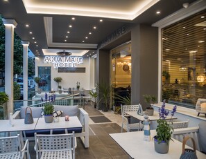 An outdoor seating area with tables and chairs, a sign for Aqua Mare Hotel, and potted plants. - Aqua Mare Hotel (Nea Propontida)