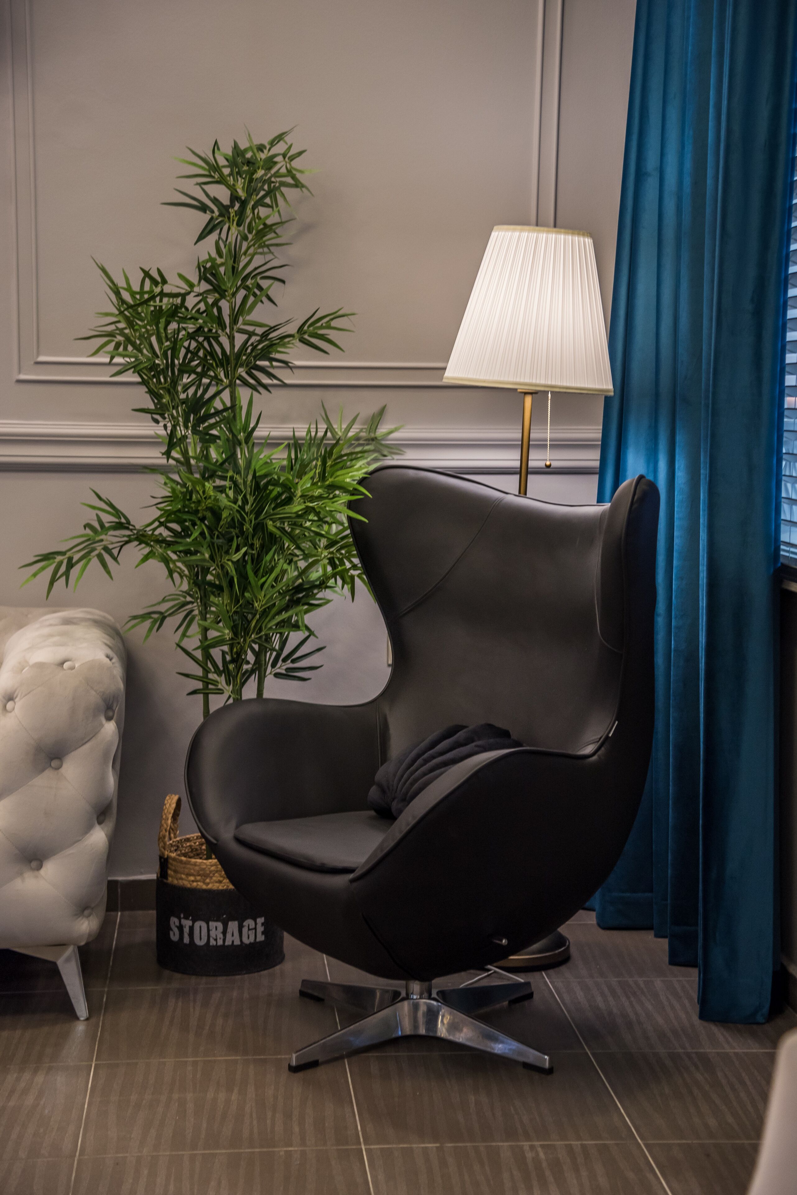 Une pièce moderne avec un fauteuil en cuir noir, une plante en pot, une lampe et un fauteuil à capitons.
