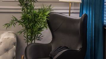 Une pièce moderne avec un fauteuil en cuir noir, une plante en pot, une lampe et un fauteuil à capitons.