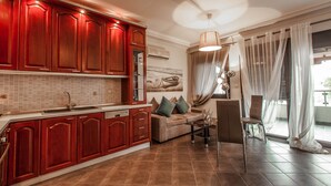 A modern kitchen with red cabinetry, a large island, and a dining area with a sofa and chairs. - Aqua Mare Sea Side (Nea Propontida)
