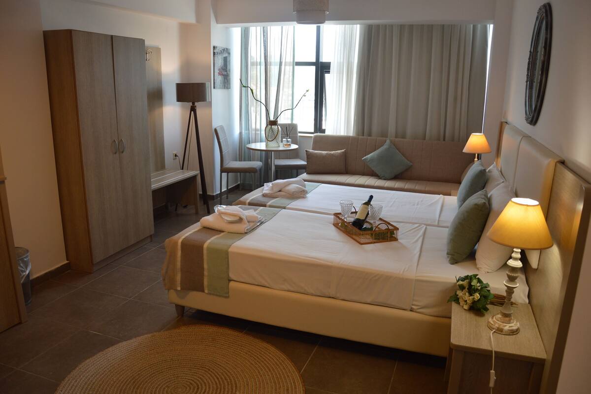 Una habitació d'hotel amb un llit gran, un sofà, una taula petita amb una làmpada i un armari.