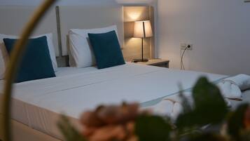 Una cama bien hecha con sábanas blancas y dos almohadas turquesa, una mesita de noche con lámpara y un enchufe en la pared.
