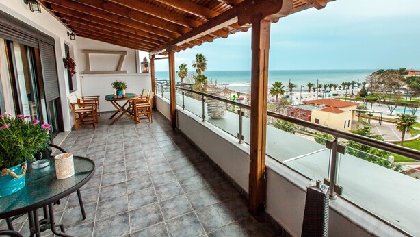 A balcony with a view of the beach, wooden furniture, and a table with a potted plant. - Aqua Mare Sea Side (Nea Propontida)