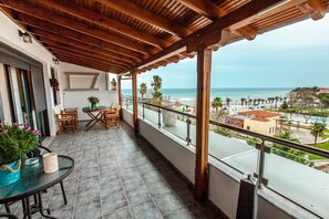 A balcony with a view of the beach, wooden furniture, and a table with a potted plant. - Aqua Mare Sea Side (Nea Propontida)