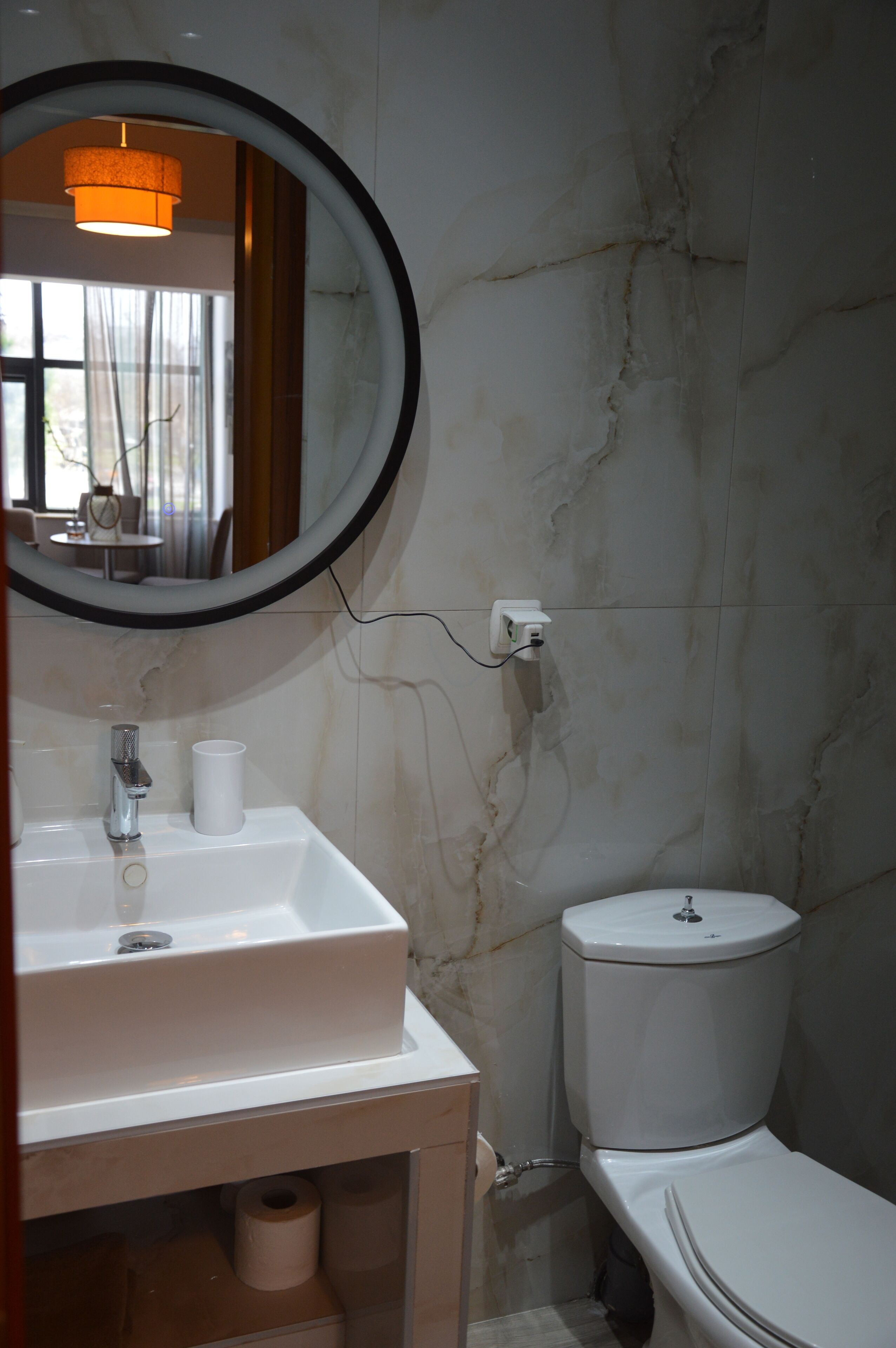 A bathroom with a white sink, a mirror, a toilet, and a roll of toilet paper.