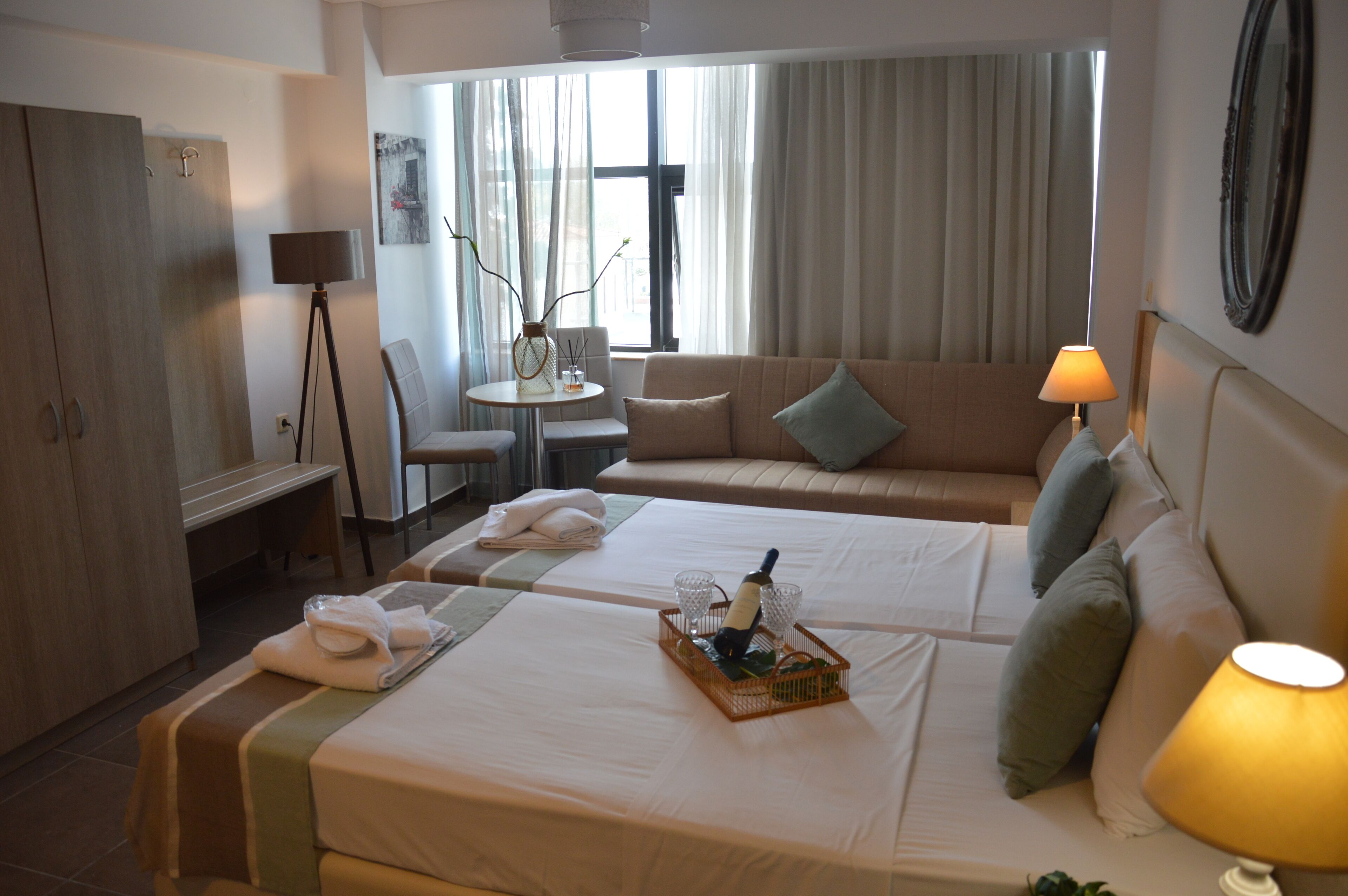 A hotel room with two beds, a sofa, a dining table, and a lamp.