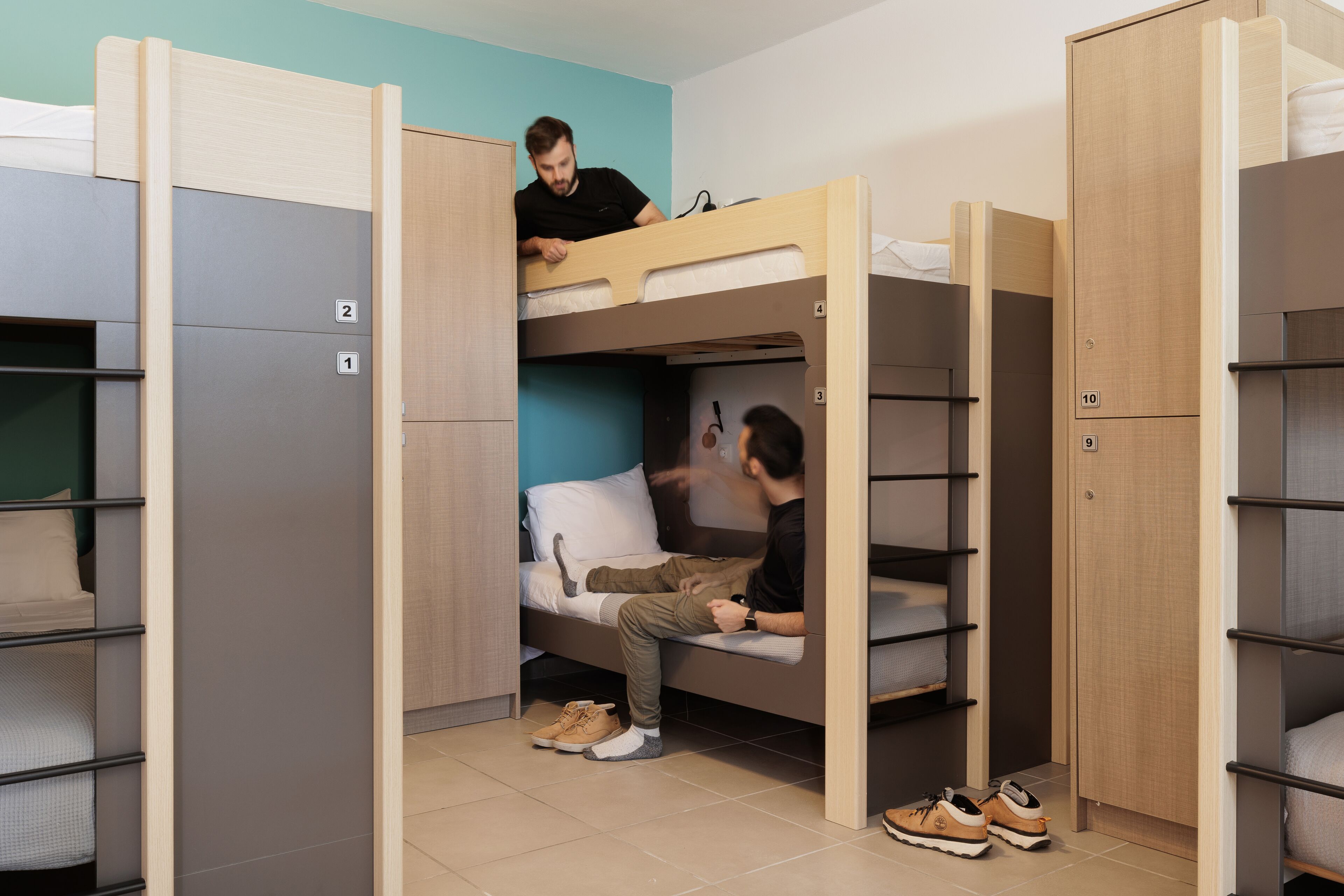 A dormitory room with bunk beds, a desk, and a wardrobe.