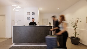 A hotel reception area with a modern design, featuring a reception desk, multiple wall clocks, and a potted plant. - Local Hostel & Suites (Corfu)