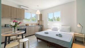 A modern hotel room with a bed, bedside table, and a small kitchen area including a sink and cabinets. - Local Hostel & Suites (Corfu)