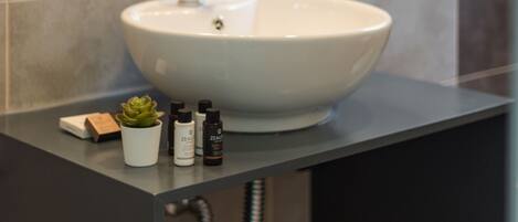 Une salle de bain avec un lavabo blanc, une petite plante en pot et quelques articles de toilette posés sur le comptoir.