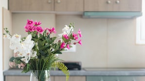 A modern kitchen with wooden cabinets, a round dining table with four stools, and a vase with pink and white flowers. - Local Hostel & Suites (Corfu)