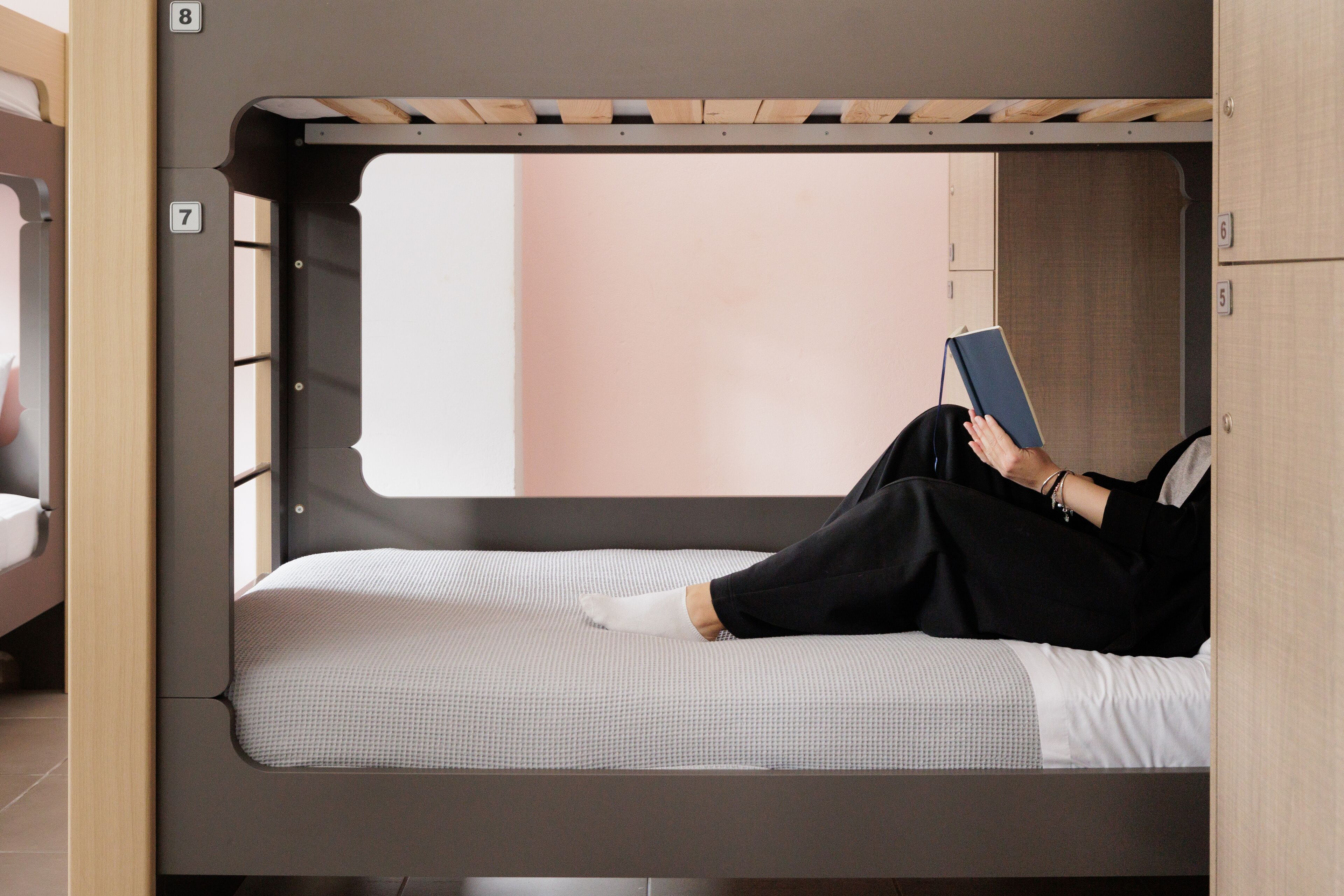 A bunk bed with a person lying on the lower bunk reading a book.