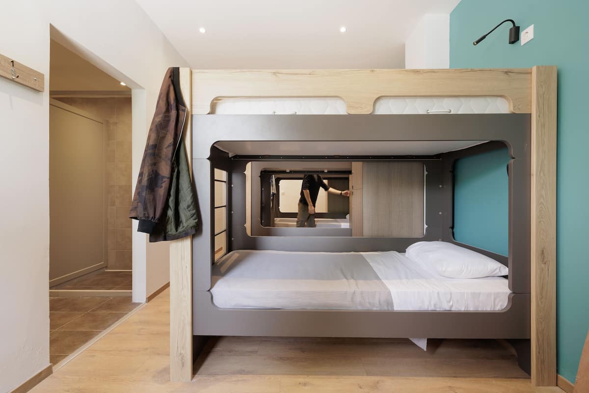 Una cama litera con cabecera de madera, un espejo y un perchero.