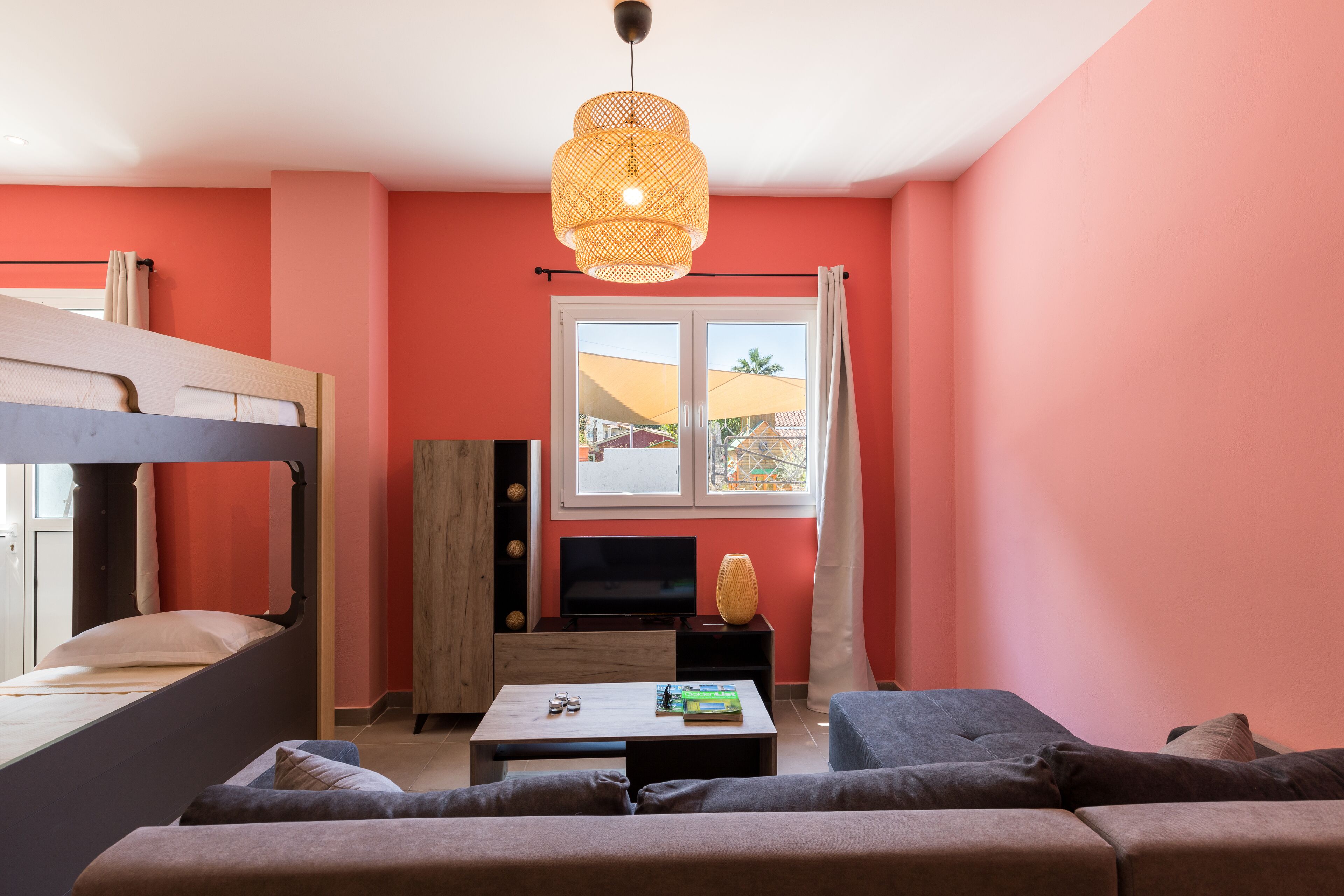 A room with a bunk bed, a sofa, a coffee table, a TV, and a window with curtains.
