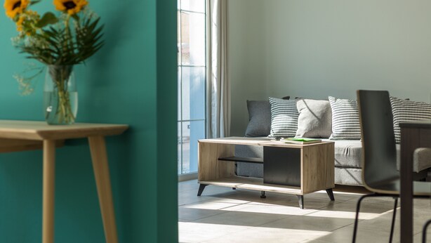 A modern living room with a wooden coffee table, a sofa with patterned cushions, and a vase of sunflowers on a side table. - Local Hostel & Suites (Corfu)
