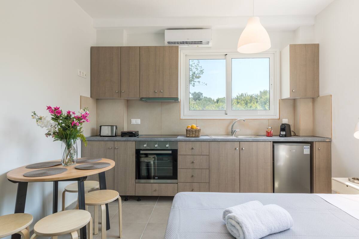 Una cocina moderna con armarios de madera, horno empotrado y lavavajillas. Hay una zona de comedor con una mesa y sillas, y una ventana que proporciona luz natural.