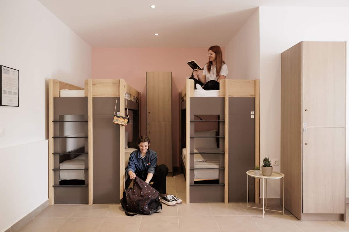 Una habitación con literas, una mesita con una planta y una persona sentada en el suelo.