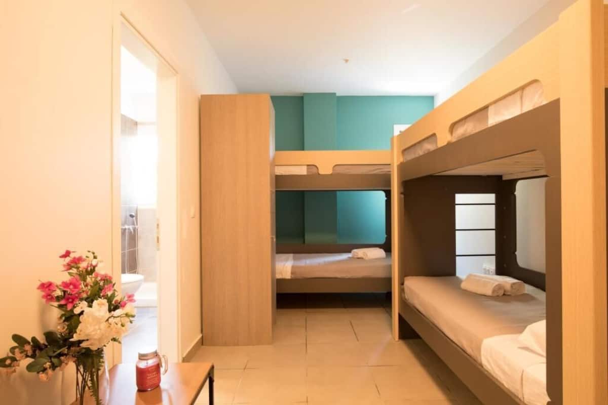 Una habitación con literas, una mesa de madera con un florero y vista al baño.