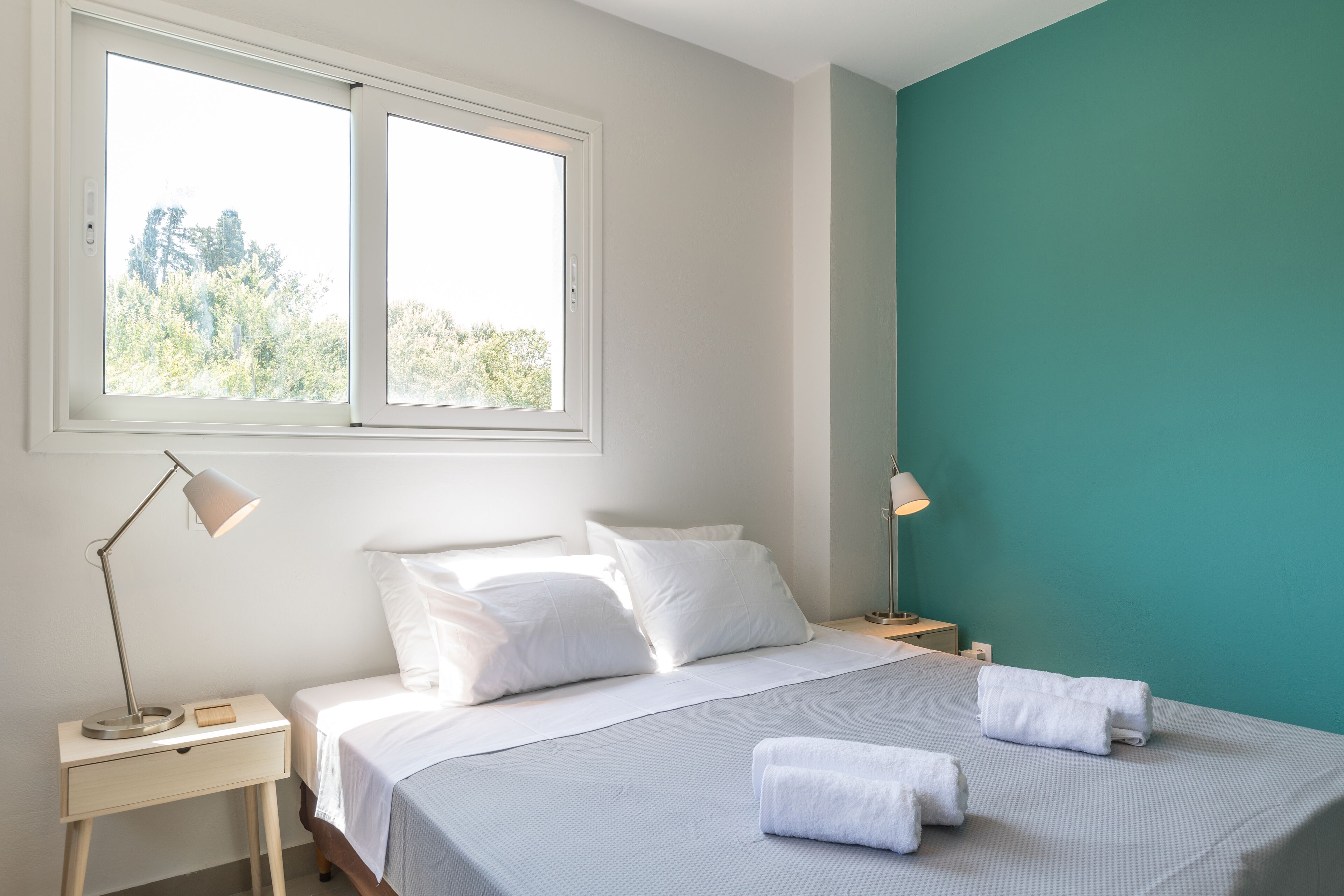 Un dormitorio con cama, dos mesitas de noche, una ventana y una pared de acento color verde azulado.