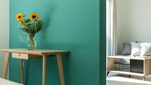 A teal-colored wall, a wooden desk with a vase of flowers, and a modern sofa with cushions. - Local Hostel & Suites (Corfu)