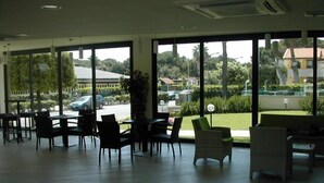 A spacious indoor area with large windows offering views of a parking lot and greenery outside. - Hotel Flora (Bibbona)