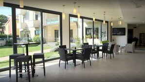 A modern indoor dining area with large windows, wicker furniture, and pendant lighting. - Hotel Flora (Bibbona)