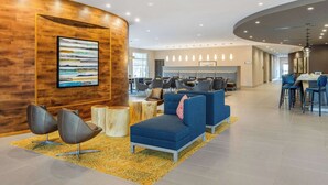 Un vestíbulo moderno con un revestimiento de madera, un cuadro abstracto de gran tamaño y un área de descanso con sofás y sillones azules.