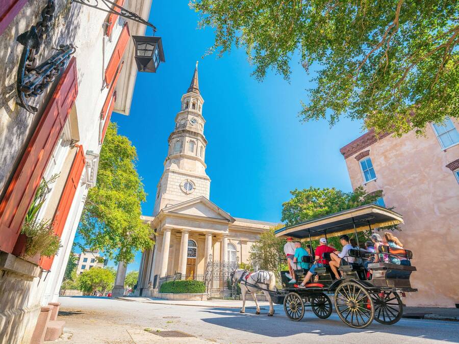 A horse-drawn carriage on a street with historic buildings, including a church with a steeple.