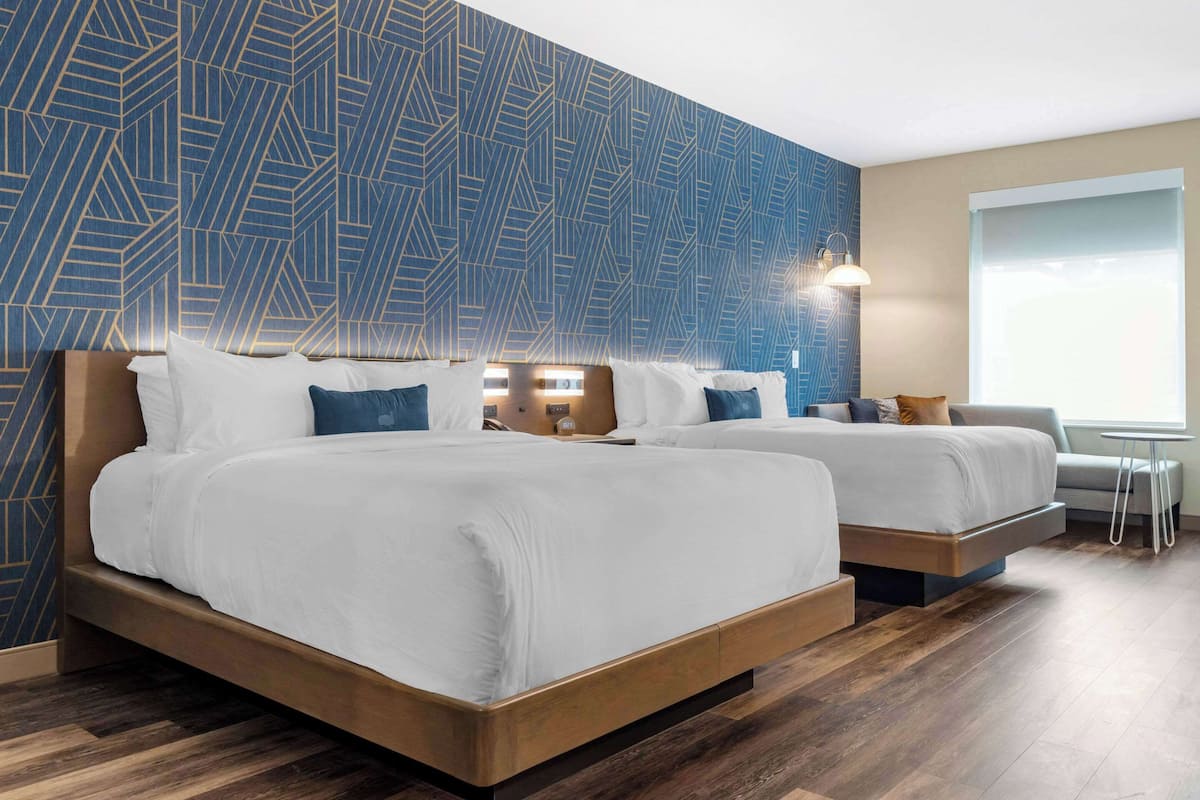 A hotel room with two beds, a large window, and a patterned wall.