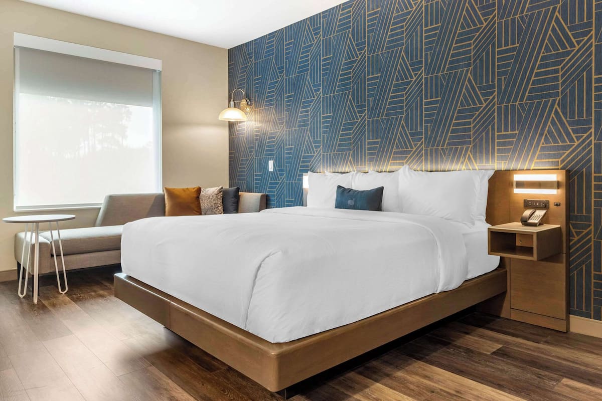 A modern hotel room with a large bed, a small round table, a sofa, and a patterned wall.