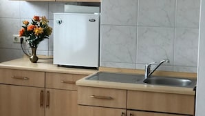 A kitchen with wooden cabinets, a white refrigerator, a sink, and a vase with flowers on the countertop. - City Hotel-Garni (Hannover)