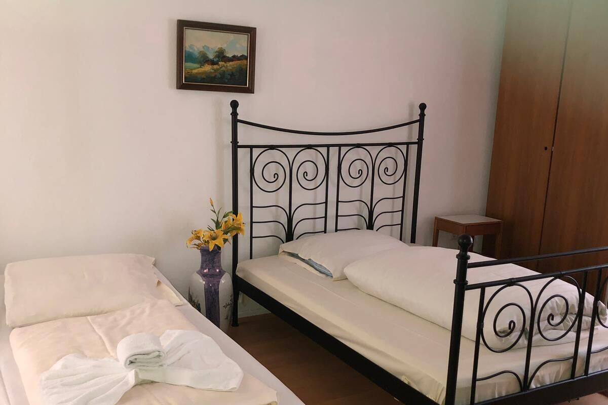 A room with two single beds, a wooden wardrobe, a small table, and a painting on the wall.