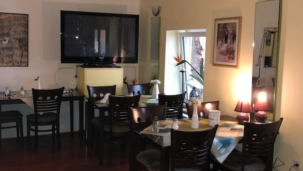A dining area with a TV mounted on the wall, a dining table set with chairs, and a window with a view of a building. - City Hotel-Garni (Hannover)