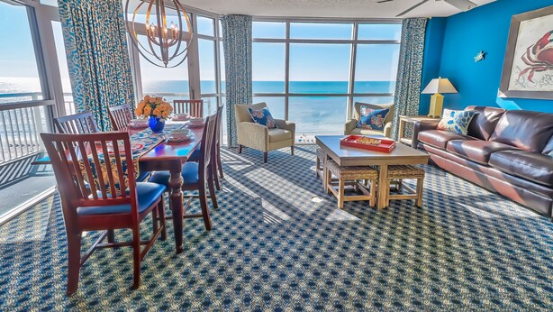A spacious living room with a large window overlooking the ocean, a dining area with a table and chairs, and a leather sofa. - ⋆𖦹NEW❀Amazing Direct OceanFront/Spacious/Pristine/Indr-WaterParks 2BR2BA2Balcs (Myrtle Beach)