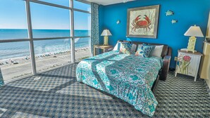 A bedroom with a large window, a bed with patterned bedding, two bedside lamps, and a ceiling fan. - ⋆𖦹NEW❀Amazing Direct OceanFront/Spacious/Pristine/Indr-WaterParks 2BR2BA2Balcs (Myrtle Beach)