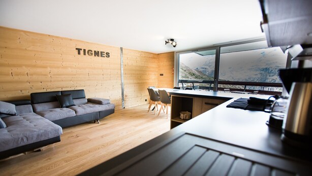 Een moderne kamer met een houten wand, een bank, een eettafel en stoelen.
