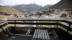 Een houten terras met een tafel en banken met uitzicht op een stadje aan de voet van een berg, met gebouwen en een sklift.