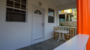 Um edifício branco com piso de pedra, uma porta branca e duas janelas.
