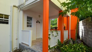 Área externa coberta com uma porta branca, pilares laranja e piso de pedra.