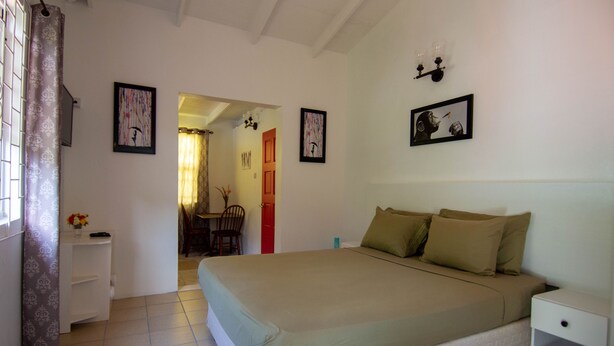 Quarto com uma cama, mesa de cabeceira, cadeira e porta que dá para outro cômodo.