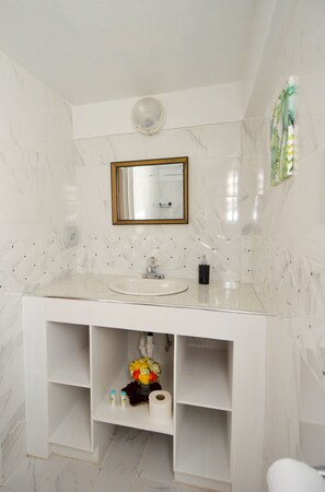 A bathroom with a marble vanity, a mirror with a gold frame, and a shower curtain with a tropical print. - Frenz (Soufrière)
