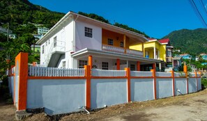 A two-story house with a balcony, surrounded by a white fence with orange accents. - Frenz (Soufrière)