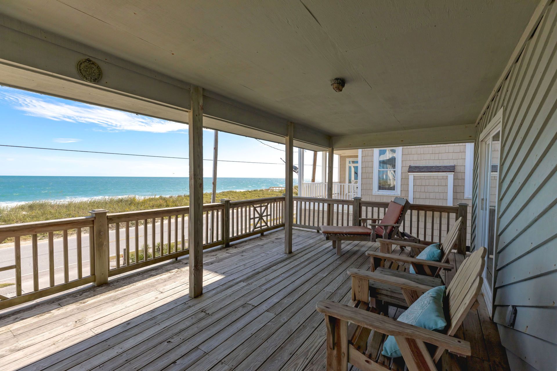 A wooden deck with a view of the ocean, a covered porch with chairs, and a building with a window.